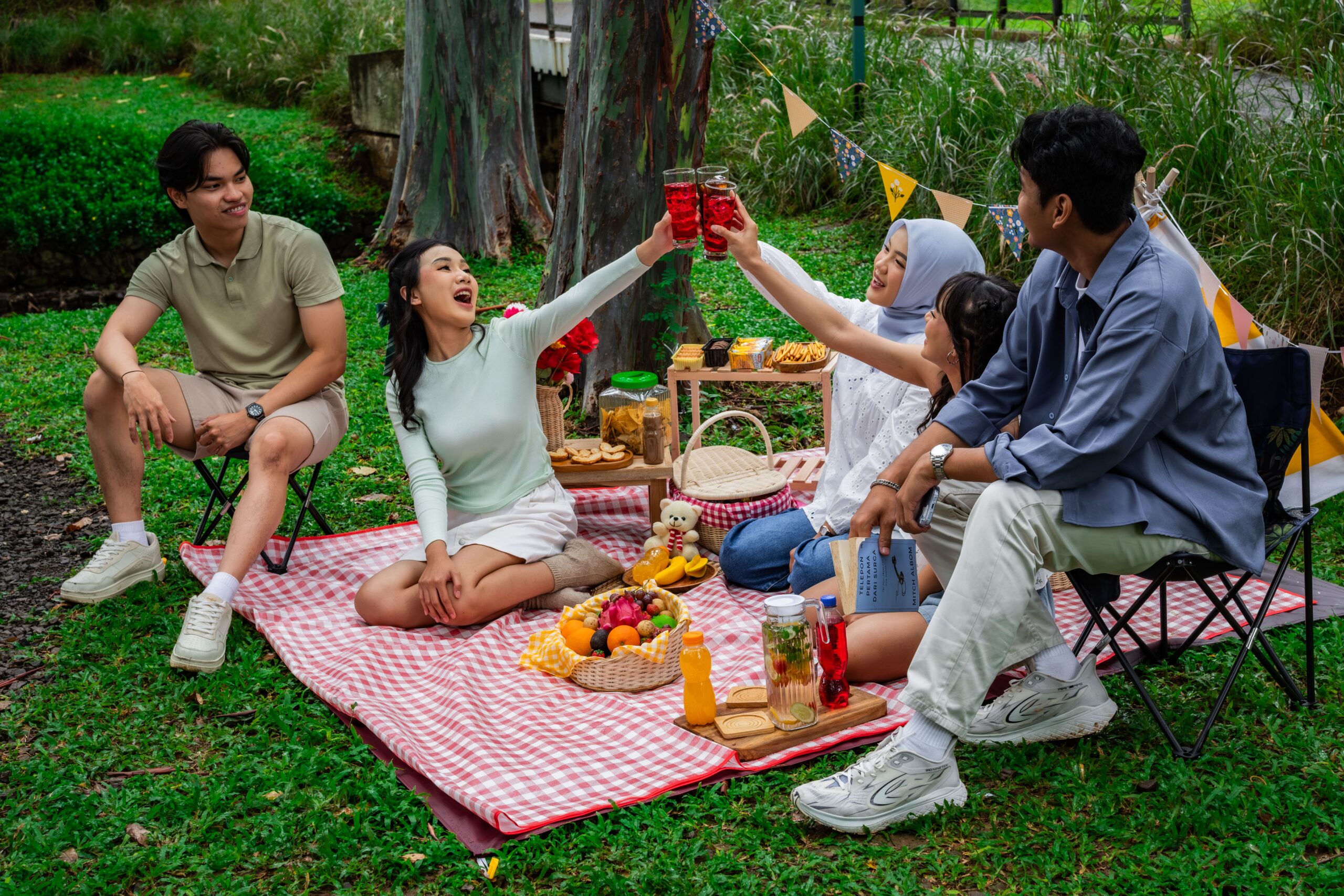 A cheerful group of friends enjoying a vibrant picnic in a lush garden setting in Indonesia.