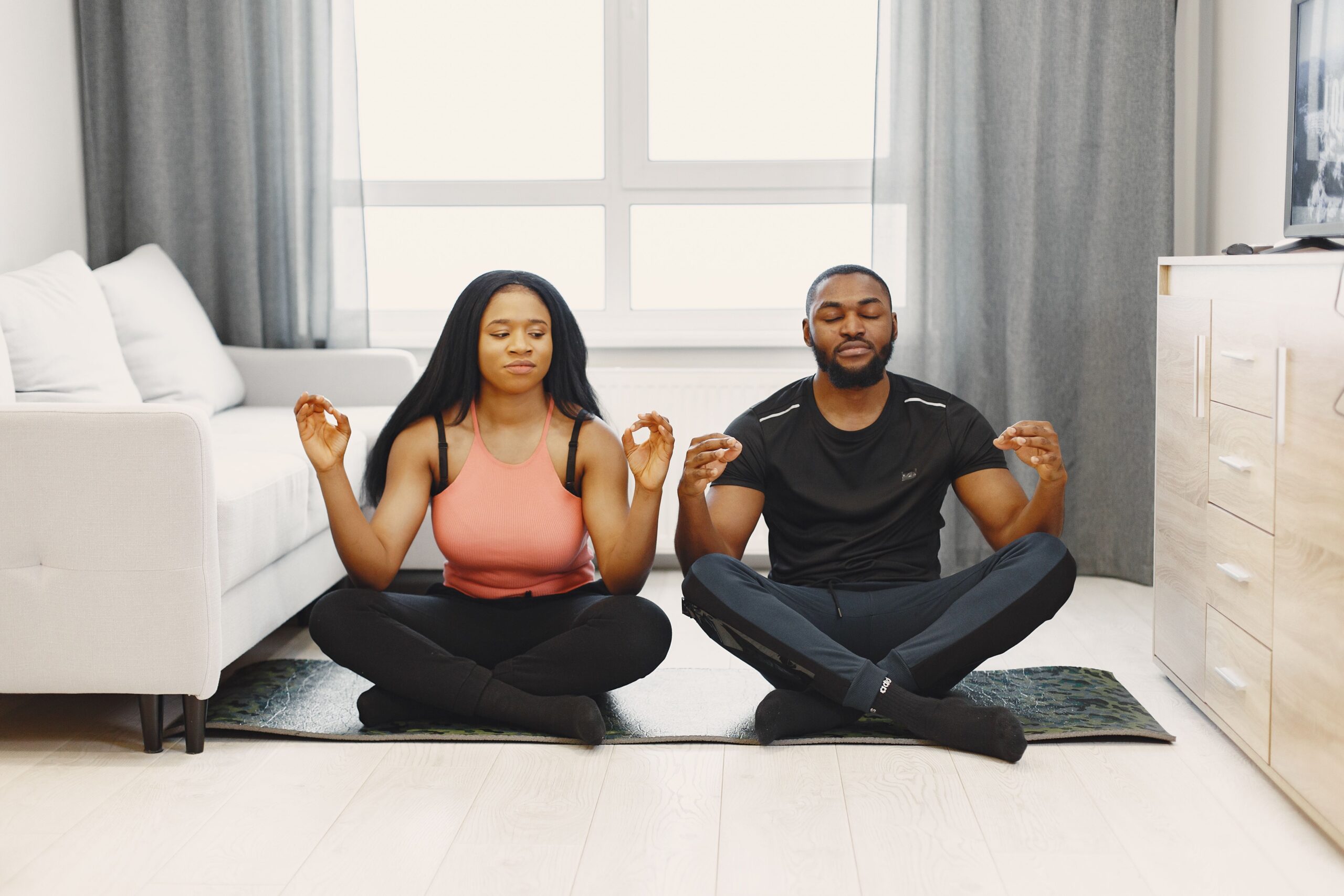 A couple meditating on yoga mats in a bright modern living room. Serenity and relaxation.